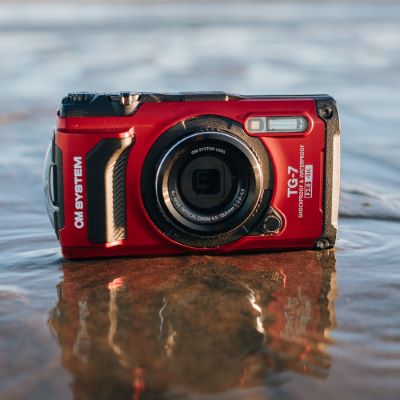 Billede af OM System TG-7 i r&oslash;d st&aring;ende i vandkanten p&aring; en strand